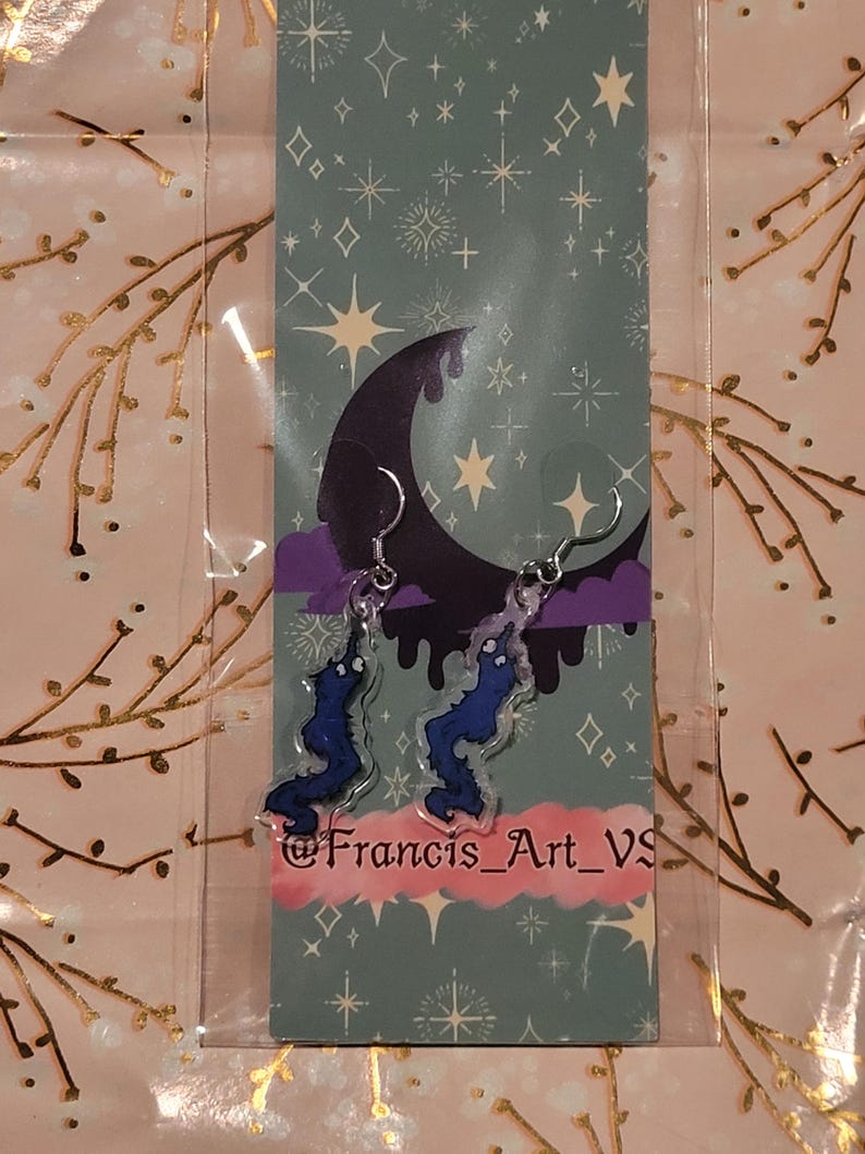 May include: A pair of blue and purple earrings shaped like a dripping, melting shape. The earrings are on a card with a crescent moon and stars. The card has the text "@Francis_Art_VS".