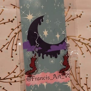 May include: A pair of red worm earrings with a dripping black moon and stars on a blue background. The earrings are on a card with the text "@Francis_Art_VS".