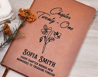 May include: A brown leather journal with the text "Chapter Twenty-One" and "Sofia Smith" in black script. A floral illustration and the phrase "Every chapter brings new memories to treasure forever" are also featured. A brown ribbon bookmark is visible.