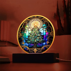 Puede incluir: Una luz nocturna de árbol de Navidad estilo vitral con marco dorado y base negra. El árbol es verde con luces de colores y una estrella en la parte superior.