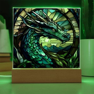 May include: A stained glass style night light featuring a green dragon with a detailed design. The dragon is set against a background of mountains and foliage.