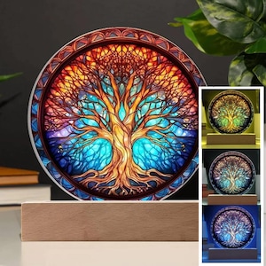 May include: A stained glass tree of life design with a colorful, swirling pattern of blue, green, orange, and purple. The design is illuminated by a light source, creating a warm glow. The tree of life is mounted on a wooden base.