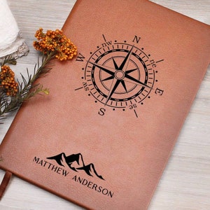 May include: A brown leather journal with a compass and mountain design. The journal is personalized with the name "MATTHEW ANDERSON".