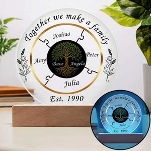 May include: A circular acrylic plaque on a wooden base featuring a central black circle with a gold tree illustration. The text reads Together we make a family, Est. 1990, and includes the names Joshua, Peter, Angela, Dave, Julia, and Amy.