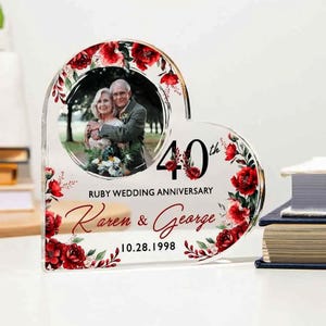 May include: Heart-shaped acrylic photo frame with a picture of a couple. The frame is decorated with red floral accents and the text "40th Ruby Wedding Anniversary" with the names "Karen & George" and the date "10.28.1998".