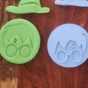 May include: A set of eight cookie cutters in blue and green plastic, featuring Harry Potter themed designs. The cutters include the Hogwarts crest, Harry Potter's glasses, a sorting hat, and a wizard's hat.