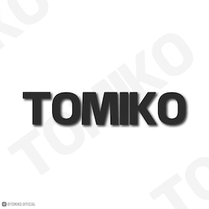 Puede incluir: La palabra "TOMIKO" en letras negritas de color gris oscuro con un sutil efecto de sombra, centrada sobre un fondo blanco. El nombre de usuario de Instagram "@TOMIKO.OFFICIAL" está en la esquina inferior izquierda, en una fuente más pequeña y gris.