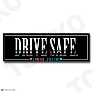 Puede incluir: Pegatina negra y blanca con el texto "DRIVE SAFE" en una fuente blanca en negrita con un efecto rayado. Debajo del texto hay un corazón rosa más pequeño, el texto "SOMEONE LOVES YOU" y un corazón azul.