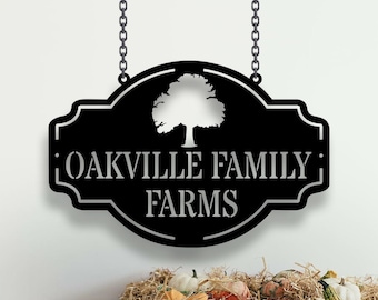 May include: Black metal sign with a white silhouette of a tree and the text "Oakville Family Farms" hanging from a chain.