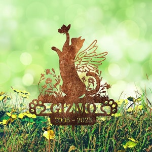 May include: A rusty metal memorial garden stake featuring a cat with wings reaching up to a butterfly. The stake has the name "Gizmo" and the dates "2005-2023" engraved on it. The stake is surrounded by green grass and yellow flowers.