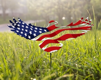 Può includere: Una silhouette di aquila in metallo con il design della bandiera americana, in piedi in un campo erboso. L'aquila guarda a destra con le ali spiegate.