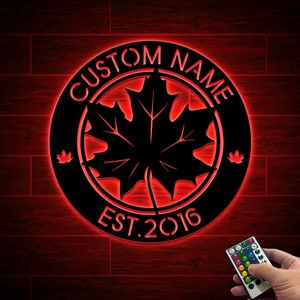 May include: Black metal sign with a red maple leaf design and the text "CUSTOM NAME EST. 2016". The sign is illuminated with red LED lights and comes with a remote control.
