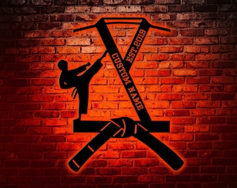 May include: Black silhouette of a martial arts figure with crossed black belts, a knot in the center, and the text "CUSTOM NAME EST. 2019". The image is on a red brick wall background.