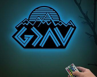 May include: A blue neon sign with the word "G.O.A.T" in a mountain range design. The sign is illuminated with a blue glow and has a remote control for changing colors.