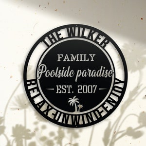Puede incluir: Se&ntilde;al de metal negro con el texto "The Wilker Family Poolside Paradise Est. 2007 Relax Unwind Enjoy" en un c&iacute;rculo con palmeras.