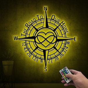 May include: A black compass with a yellow glow, featuring the text "The Road To Our Home" and a heart with an infinity symbol. The compass has a black background with white numbers and markings.