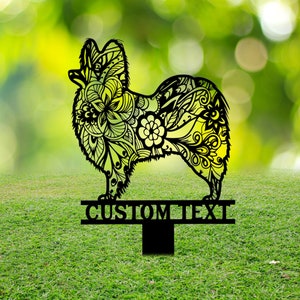 May include: Black metal silhouette of a Papillon dog with intricate floral designs. The silhouette is mounted on a metal stake with a sign that reads "CUSTOM TEXT".