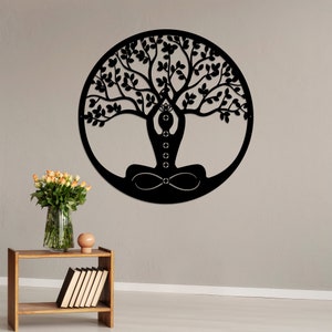 K&ouml;nnte beinhalten: Schwarze Wandkunst aus Metall, die einen Lebensbaum mit einer Person darstellt, die im Zentrum in einer Yoga-Pose sitzt. Der Baum hat komplizierte &Auml;ste und Bl&auml;tter.