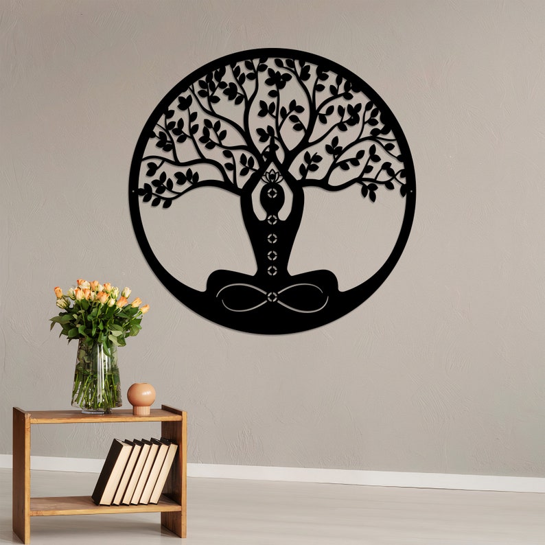 K&ouml;nnte beinhalten: Schwarze Wandkunst aus Metall, die einen Lebensbaum mit einer Person darstellt, die im Zentrum in einer Yoga-Pose sitzt. Der Baum hat komplizierte &Auml;ste und Bl&auml;tter.
