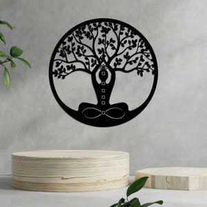 K&ouml;nnte beinhalten: Schwarze Wandkunst aus Metall, die einen Lebensbaum mit einer Person darstellt, die im Zentrum in einer Yoga-Pose sitzt. Der Baum hat viele &Auml;ste und Bl&auml;tter.