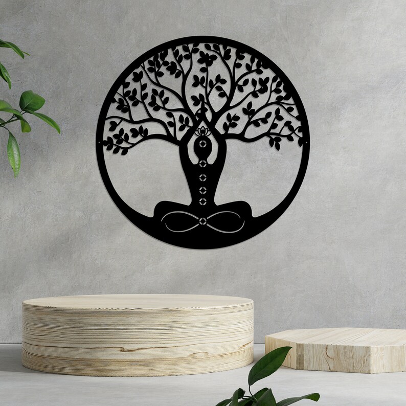 K&ouml;nnte beinhalten: Schwarze Wandkunst aus Metall, die einen Lebensbaum mit einer Person darstellt, die im Zentrum in einer Yoga-Pose sitzt. Der Baum hat viele &Auml;ste und Bl&auml;tter.