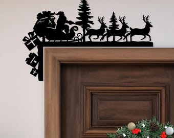 May include: Black metal Christmas decoration featuring Santa Claus in a sleigh pulled by reindeer, with gifts and trees. The silhouette design is mounted on a door frame, creating a festive holiday display.