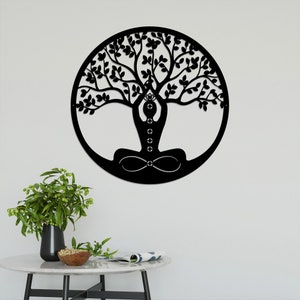 K&ouml;nnte beinhalten: Schwarze Wandkunst aus Metall mit einem Lebensbaum-Design, in dessen Mitte eine Person meditiert. Der Baum hat komplizierte &Auml;ste und Bl&auml;tter, und die Person befindet sich in einer Yoga-Pose.