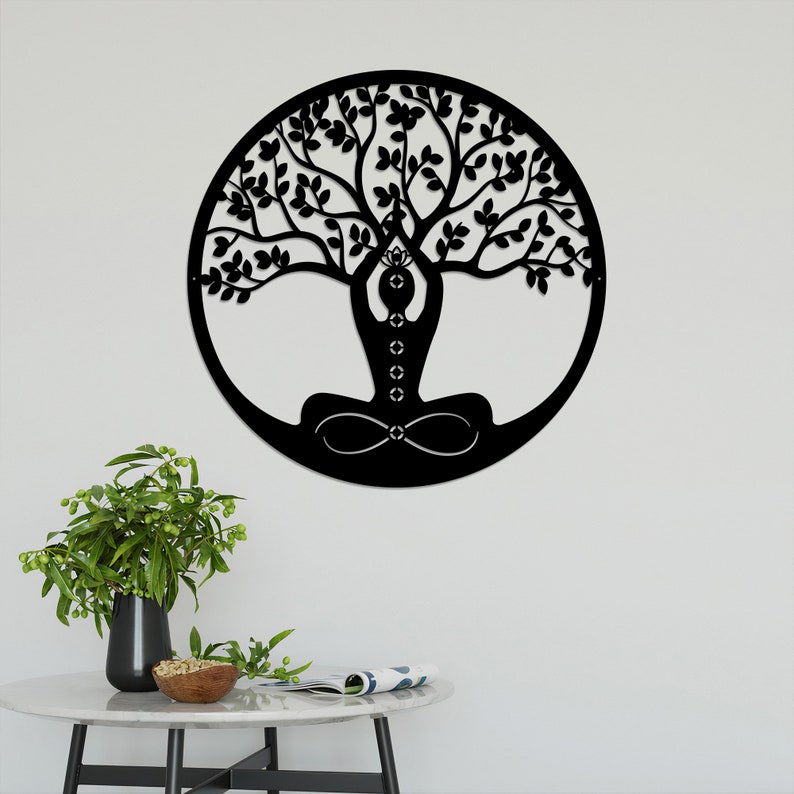 K&ouml;nnte beinhalten: Schwarze Wandkunst aus Metall mit einem Lebensbaum-Design, in dessen Mitte eine Person meditiert. Der Baum hat komplizierte &Auml;ste und Bl&auml;tter, und die Person befindet sich in einer Yoga-Pose.