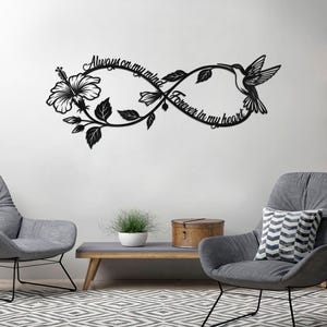 May include: Black metal wall art featuring an infinity symbol design with a hibiscus flower, leaves, and a hummingbird. The text reads "Always on my mind" and "Forever in my heart". The artwork is mounted on a white wall.