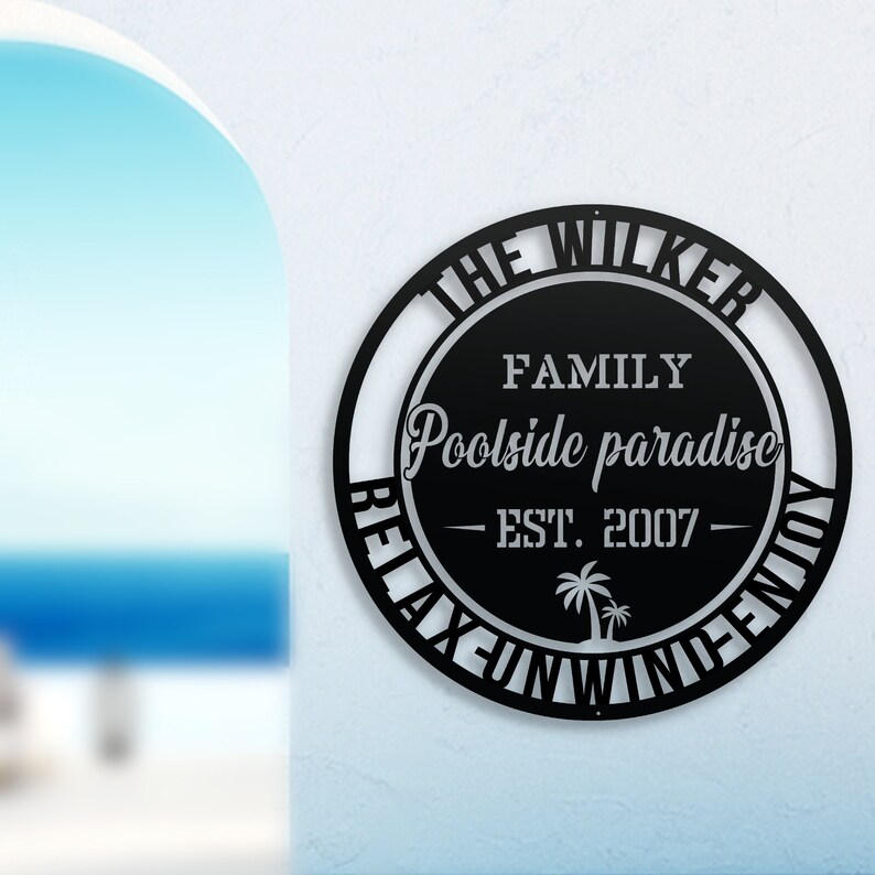Puede incluir: Se&ntilde;al de metal negro con el texto "The Wilker Family Poolside Paradise - Est. 2007 - Relax Unwind Enjoy" en un c&iacute;rculo.