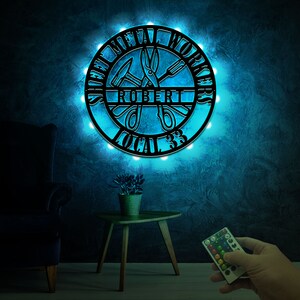 May include: A black metal sign with the words "Sheet Metal Workers" and "Local 33" around a pair of scissors and a hammer. The sign is illuminated with blue LED lights and has the name "Robert" in the center.