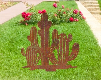May include: A metal silhouette of a group of cacti in a rusty brown color. The cacti are arranged in a cluster and are set against a green grassy background.