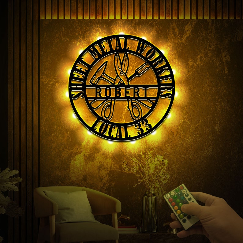 May include: A black metal sign with the words "Sheet Metal Workers Local 33" and the name "Robert" in the center. The sign is illuminated with warm white lights and features a pair of scissors and other tools.