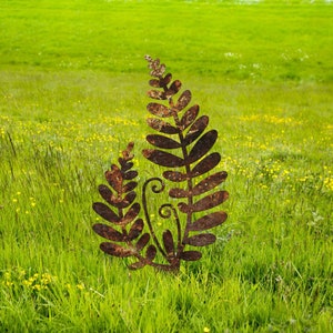 May include: A rusty metal fern sculpture with two fronds, standing in a field of green grass with yellow wildflowers.
