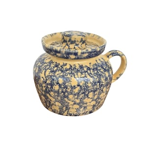 Op de afbeelding: Een keramieken pot met deksel en één handvat, voorzien van een crèmekleurige basis met een dicht, gespikkeld marineblauw spons-patroon dat het gehele buitenoppervlak bedekt, inclusief de bovenkant van het deksel en het handvat.