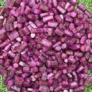 Op de afbeelding: Een grote stapel ruwe, onbewerkte, roze robijnkristallen. De kristallen zijn allemaal van verschillende grootte en vorm, maar ze zijn allemaal diep roze van kleur.