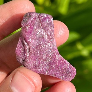 May include: A rough, pink ruby crystal with a natural, irregular shape. The crystal has a deep, rich pink color and a slightly translucent appearance.