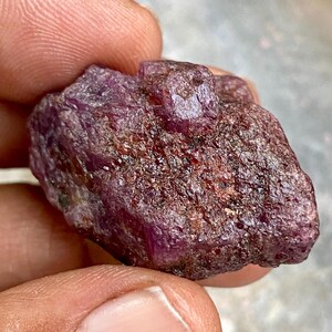 Pode incluir: Uma gema de rubi vermelho escuro bruto com um acabamento natural não polido.