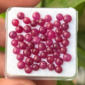 May include: A collection of 40 round, red ruby gemstones in a white box. The gemstones are all approximately the same size and have a smooth, polished finish.