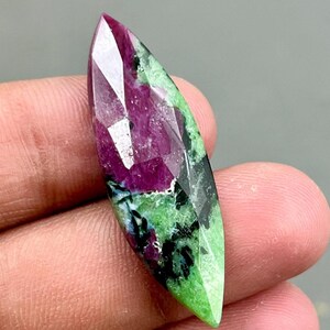 Può includere: Un cabochon di pietra preziosa verde e rosa con taglio sfaccettato. La pietra preziosa è di un verde vibrante con inclusiones rosa e nere.
