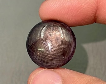 Pode incluir: Uma gema redonda de cor púrpura escura com um padrão em forma de estrela no centro. A gema é polida e tem uma superfície lisa.