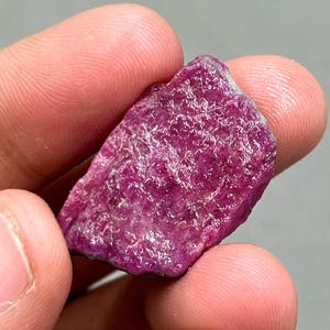 May include: A rough, pink ruby gemstone with a natural, unpolished finish. The ruby is a deep, rich pink colour and has a slightly translucent appearance.