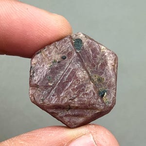 以下が含まれることがあります： 六角形の形状をした深紅色のルビーの結晶。表面は粗く、質感がある。結晶には黒いインクルージョンがいくつかある。