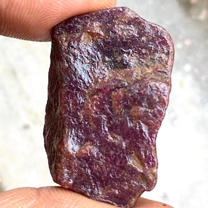 Può includere: Una pietra preziosa grezza di colore viola scuro con una forma leggermente irregolare. La pietra preziosa ha una superficie lucida e lucidata.