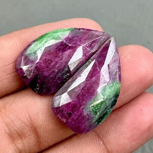Peut inclure: Deux cabochons de pierres précieuses vertes et roses avec une taille facetée. Les cabochons sont en forme de poire et ont une apparence translucide.