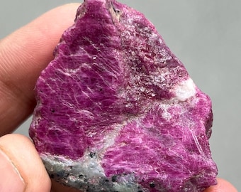 May include: A rough, pink ruby crystal with a dark gray and white matrix. The crystal has a deep, rich pink color and is translucent.
