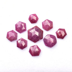 May include: A selection of faceted, hexagonal gemstones in various sizes. The gems are a deep, rich red colour and are arranged on a white background. The facets catch the light, creating a sparkling effect. These gemstones are suitable for jewellery making.