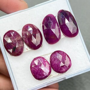 Puede incluir: Seis piedras preciosas ovaladas facetadas en una caja blanca. Las piedras preciosas son de color rosa intenso.