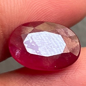 Puede incluir: Una piedra preciosa ovalada de color rojo intenso con un corte facetado.