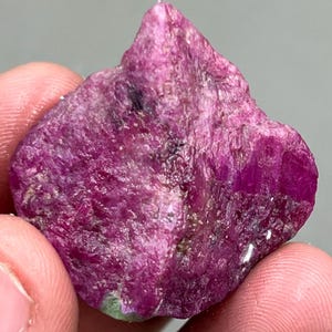 Può includere: Un grande cristallo di rubino rosa grezzo con una tonalità rosso intenso. Il cristallo ha una superficie naturale non lucidata ed è un bellissimo esempio di questa gemma.